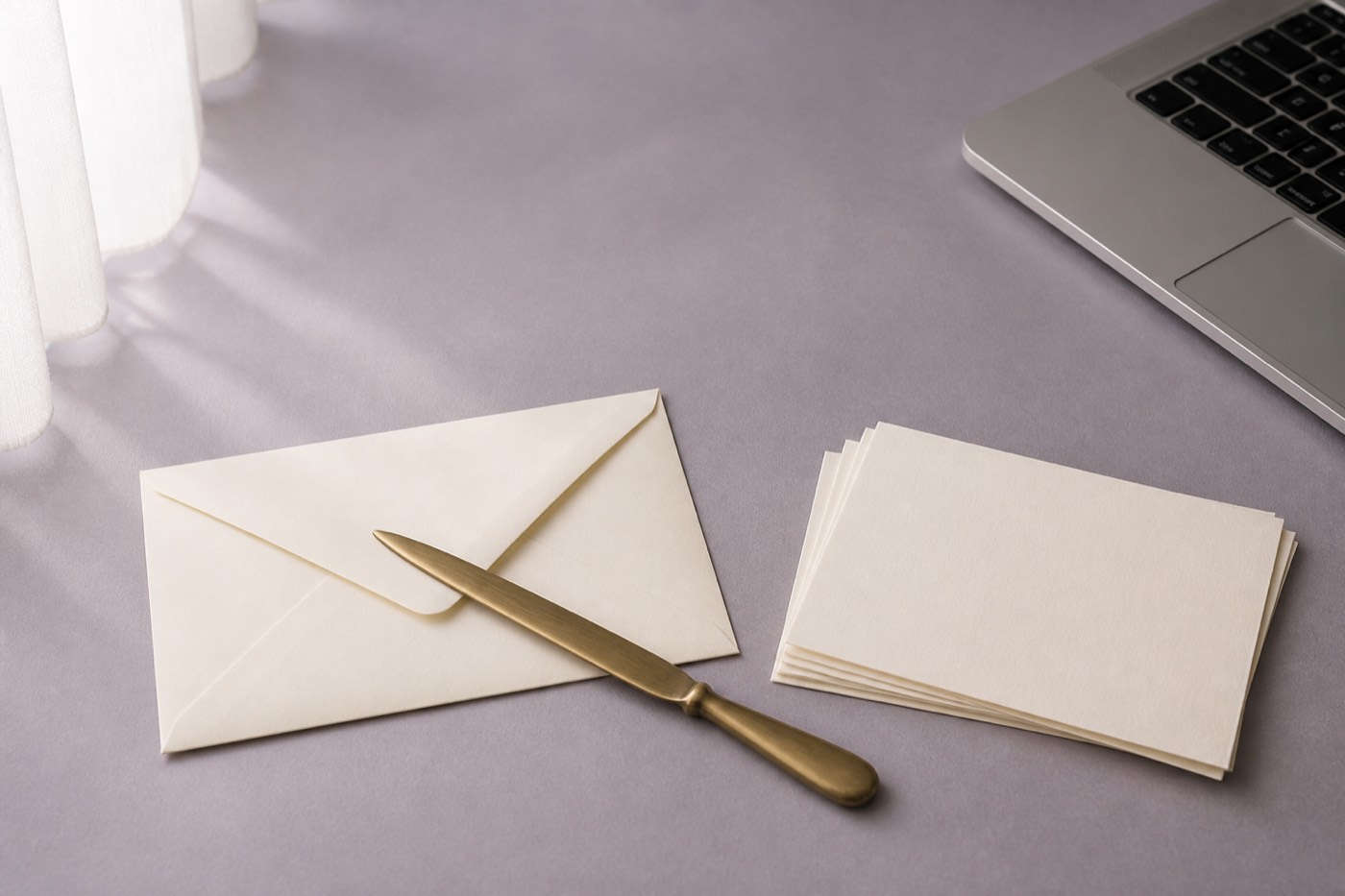 Enveloppe crème, coupe-papier en laiton et cartes de correspondance vierges sur un bureau
